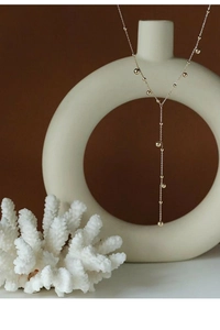 Detail of 18k gold plated Y-shaped necklace with beads hanging on a minimalist vase