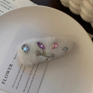 Close-up of white plush hair clip with colorful gemstones and silver metal rose