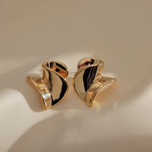 Elegant gold spiral earrings with wrinkled texture on soft beige silk background