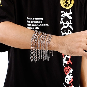 Close-up of stacked silver stainless steel Figaro and Cuban chain bracelets on wrist