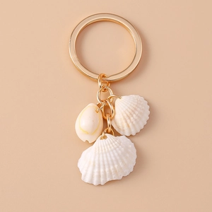 Golden keychain with natural seashells and scallops on a minimalist beige background