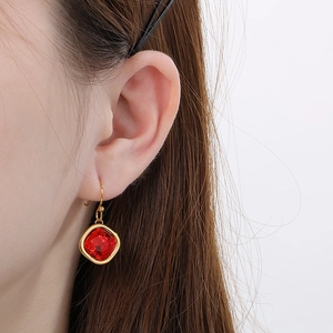 Macro shot of square red gemstone earrings with gold plating worn on model's ear