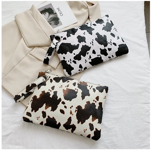 Close-up of cow pattern envelope clutch bags with leather texture and metal zipper detail