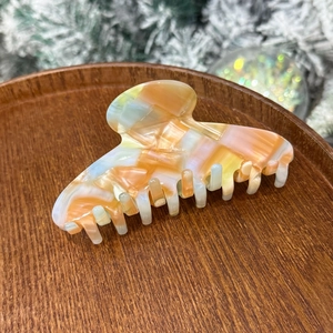 Detail of orange marble acetate hair claw clip with golden script on wooden tray
