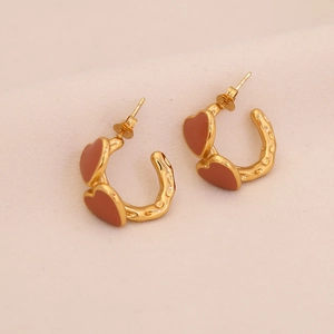Golden C-shaped heart earrings with reddish-brown enamel inlay on pink background