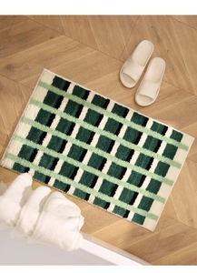 Détail d'un tapis de bain moelleux à carreaux verts et beige sur parquet à chevrons