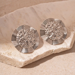 Macro shot of silver metal geometric earrings with molten lava texture on natural stone
