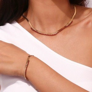 Golden herringbone necklace and bracelet set with red zircons shown on a model