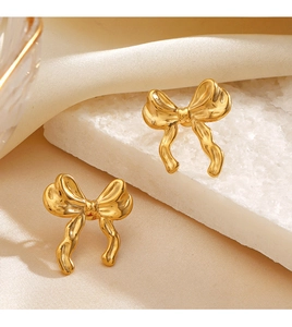 Detail of 18K gold plated bow earrings on white textured stone and beige velvet base