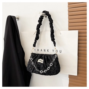 Detail of black pleated cloud bag with elegant floral chain and soft fabric texture
