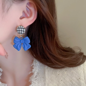 Close-up of blue bow earrings with houndstooth studs worn by a model in soft light