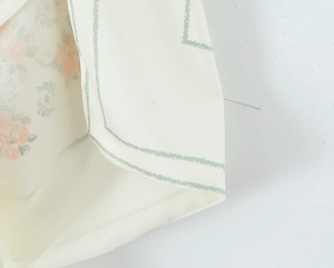 Macro view of floral satin fabric with orange print and green striped edge detailing
