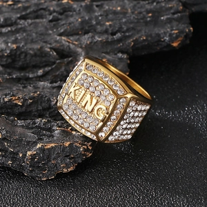 Close-up of gold-plated KING signet ring with inlaid crystals on a dark stone background