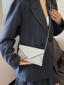 Silberne gewebte Briefumschlagtasche mit Goldkette über grauem Blazer getragen
