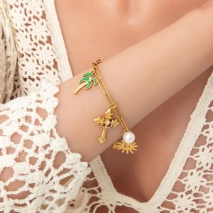 Close-up of gold charm bracelet with pearl, green coconut tree, cross and sun pendants