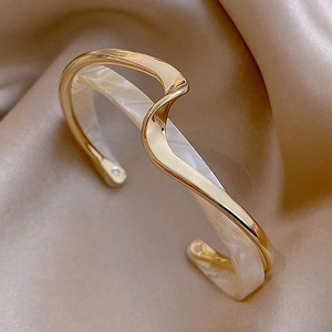 Detailed macro view of gold-plated wavy double-layer cuff with cream marble acrylic