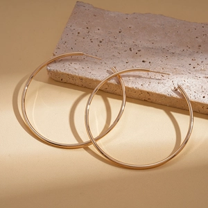 Macro shot of large gold geometric twisted round earrings on a beige textured stone base