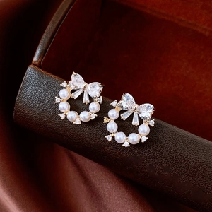 Macro shot of bow pearl earrings featuring sparkling zircon inlay and elegant gold plating
