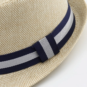 Detalle de un sombrero de paja beige con cinta decorativa de rayas azul marino y blanco