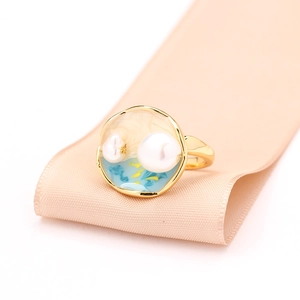 Détail d'une bague dorée avec résine bleue et beige et perle sur un ruban rose