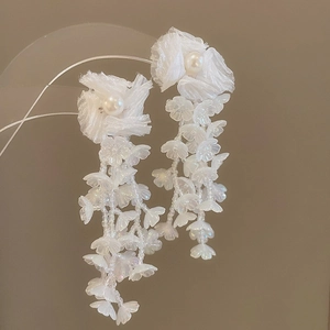 Macro detail of white chiffon flower earrings with central pearl and beaded floral tassels