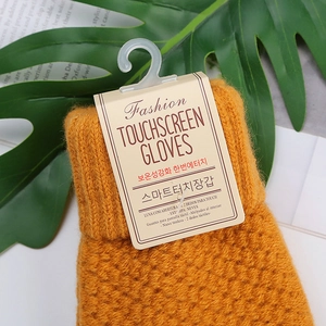 Close-up of tan knit touchscreen gloves with brand tag against a natural leaf background