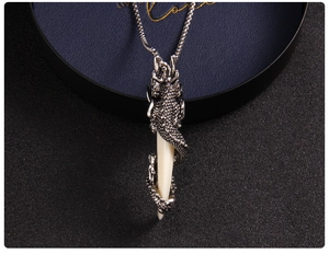 Detailed view of a dark metal dragon pendant wrapped around a white faux fang on a chain