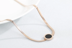 Close-up of golden flat snake chain necklace with a minimalist round black shell pendant