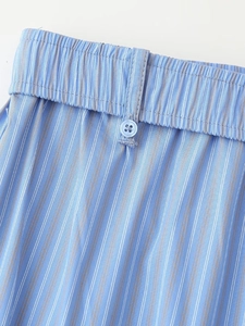 Detail of light blue striped trousers featuring elastic waistband and button accent