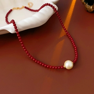 Détail d'un collier de perles rouges avec un pendentif perle sur une assiette en céramique