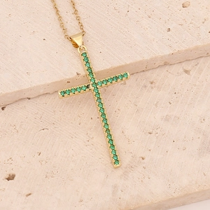 Golden cross necklace with green zircon stones on beige natural stone background