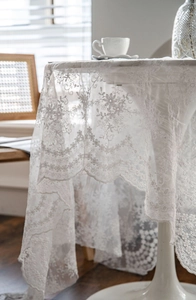 Close-up of white lace tablecloth featuring delicate floral embroidery on circular table