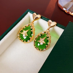 Close-up of teardrop earrings with green gemstone, star, and pearl on white lining