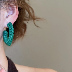 Close-up of deep green hand-woven C-shaped leather earrings with braided texture detail