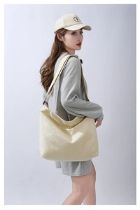 Dettaglio di una grande borsa a tracolla in tela beige con un outfit casual grigio nido d'ape