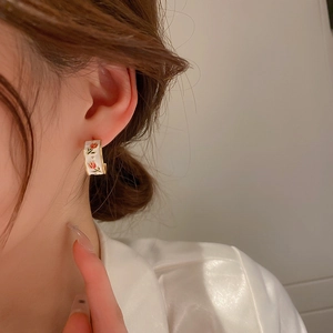 Close-up of French vintage C-shape hoop earrings featuring red tulip enamel patterns