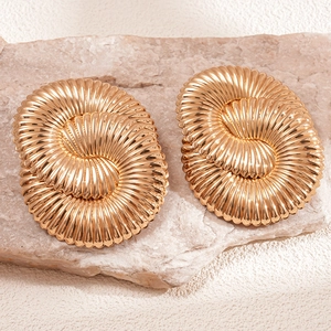 Détail macro de boucles d'oreilles spirales dorées polies sur fond de pierre