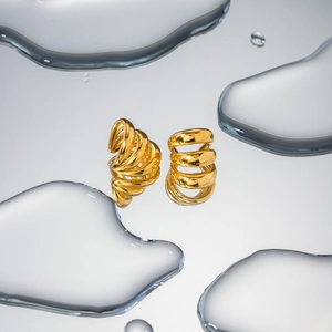 Macro shot of polished 18K gold-plated stainless steel multi-layer spiral earrings on water surface