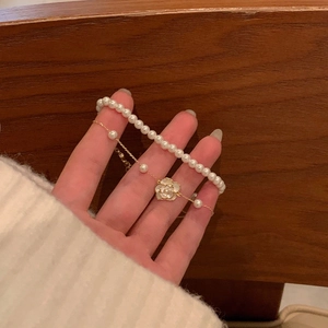 Detalle de una pulsera dorada de doble capa con perlas y un colgante de flor de camelia