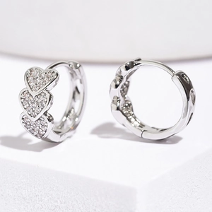 Polished silver heart hoop earrings with micro-pave cubic zirconia on white pedestal