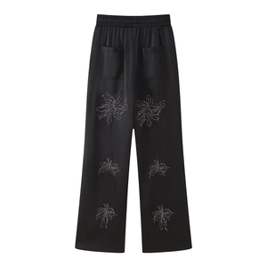 Detail of black satin wide-leg pants with elastic waist and silver floral print accents