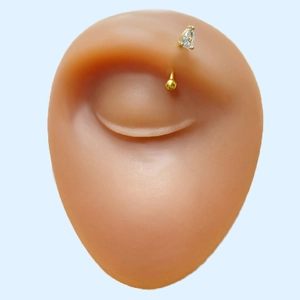 Detail of curved gold barbell eyebrow ring with drop-shaped zircon on silicone model