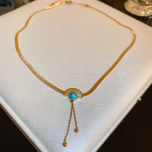Detail view of a gold fan-shaped earring with turquoise bead and delicate chain tassels