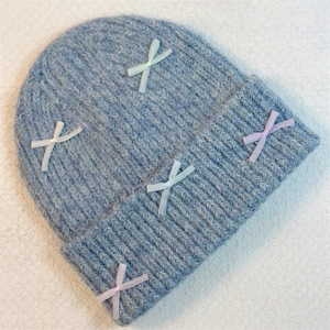 Close-up of light blue knit beanie featuring colorful pastel ribbon bows on soft fabric