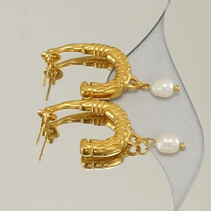 Elegant gold U-shaped earrings with baroque pearls and textured finish on a mirror base