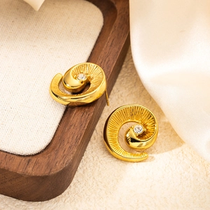 Macro detail of golden spiral stud earrings with brushed texture and small zircon stone