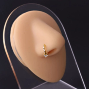 Close-up of a golden nose ring with clear gemstone inlay and a dangling heart charm