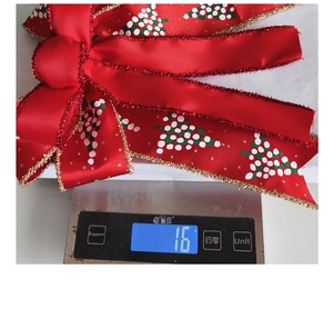 Detail shot of a festive red Christmas bow being weighed on a scale showing 16 grams