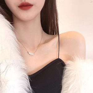 Minimalist gold necklace with three pearls shown on model in white faux fur coat