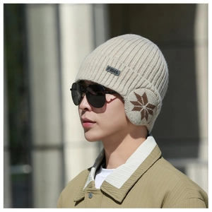 Detail of knitted winter beanie with ear flaps featuring snowflake patterns and leather logo